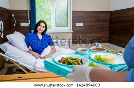 Nurse in medical coat is holding a tray with breakfast for the young female patient. Hospital food concept