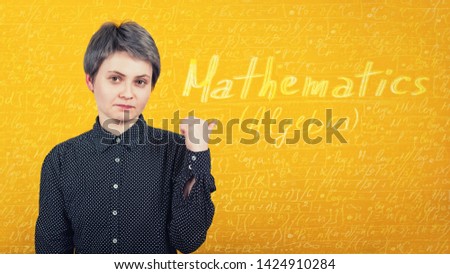 Woman student tired of learning, pointing finger to a yellow wall with written mathematics formulas and equations. Education concept, difficult process to study algebra.