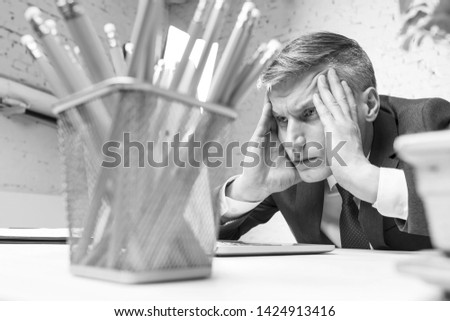 Black and White photo of Overworked mature businessman looking at laptop on desk in office