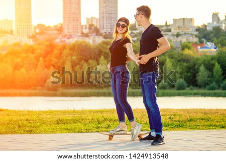 active couple in love sport skating in the summer park. beautiful woman and man have fun with a skateboard(longboard) background of a sunset by the river. guy and girl date. romance flirting concept