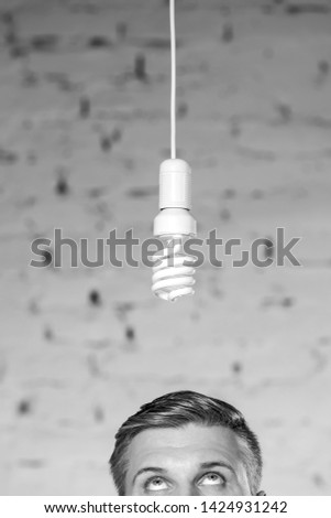 Black and White photo of High section of thoughtful mature businessman looking at energy efficient lightbulb hanging against brick wall at office