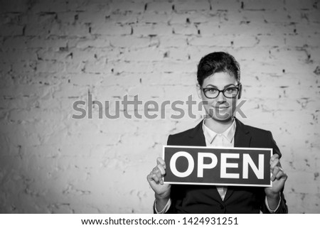 Black and White photo of Portrait of beautiful young businesswoman holding open sign placard against brick wall