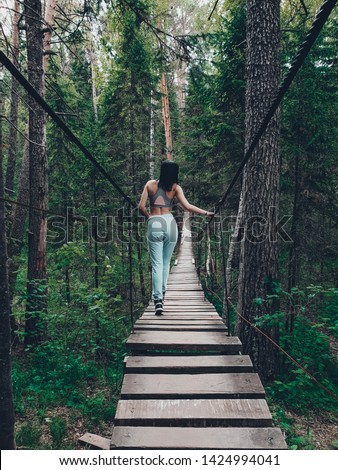 The girl goes on a suspension bridge in the forest