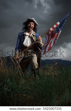 American revolution war soldier with flag of colonies over dramatic landscape. 4 july independence day of USA concept photo composition: soldier and flag. Royalty-Free Stock Photo #1425007331