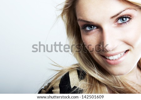 Close-up portrait of a smiling beautiful blonde caucasian woman with blue eyes, looking at camera, on a gray background with copy-space Royalty-Free Stock Photo #142501609