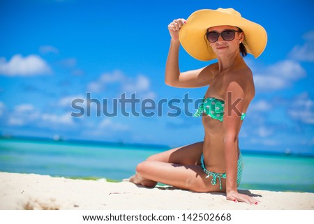 Woman sitting on beach holding beach hat enjoying summer holidays looking at the ocean. Beautiful back side of model in bikini sitting down.