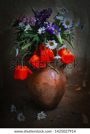 The photo was taken in 2019.The picture shows a pitcher of flowers, which stands on the table.In a jug of poppy flowers,daisies and lupins.