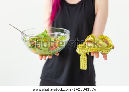 Young unidentified fitness blogger girl holding vegetable salad and measuring tape. Concept of sports lifestyle and proper nutrition.