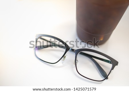 Close up oof readding glasses with plastic cup of iced black coffee on white table.