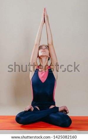 Beautiful slim fit woman coach stands in asanas on a bright rug on a beige background. Yoga practice. Useful hobby for maintaining a healthy body, wellness gymnastics