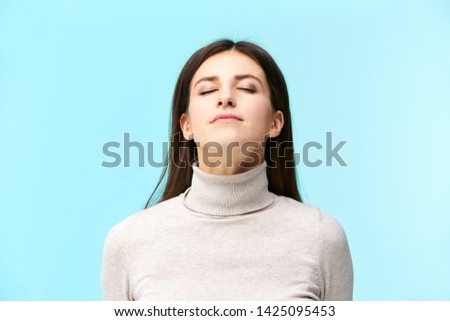 portrait of a beautiful young caucasian woman, eyes closed, smelling fragrance in the air, isolated on blue background Royalty-Free Stock Photo #1425095453