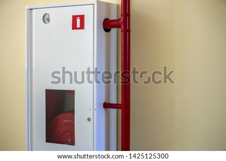White metal cabinet with fire extinguishing hose reel on light wall copy space background.