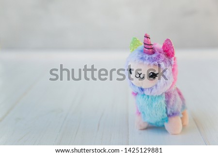 Colored plush llama unicorn on white wooden background