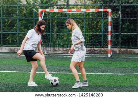 Photo of two pretty  woman playing football together on field.