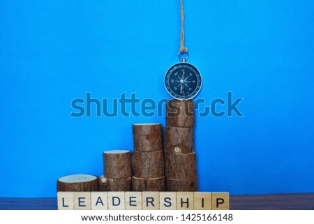 Wooden blocks arranged with the words LEADERSHIP and magnetic compass on blue background. Conceptual Image, selective focus. 