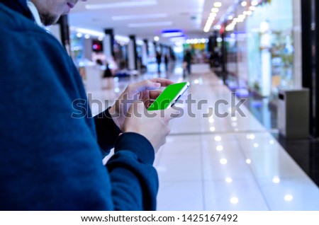 Man using mobile phone in shopping mall or airport indoor.Green blank screen in man hand 
