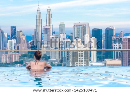 Woman relaxing in infinity swimming pool roof top looking at beautiful city skyscraper view Kuala lumpur, Malaysia