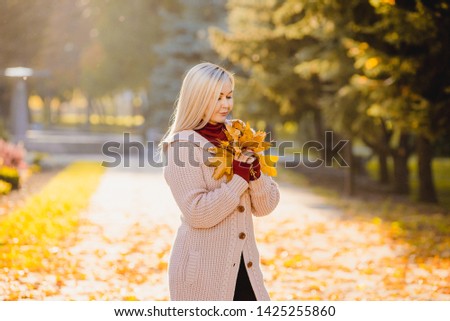 Romantic woman in the fall in the park. Stylish girl holding a golden autumn leaf near the face.