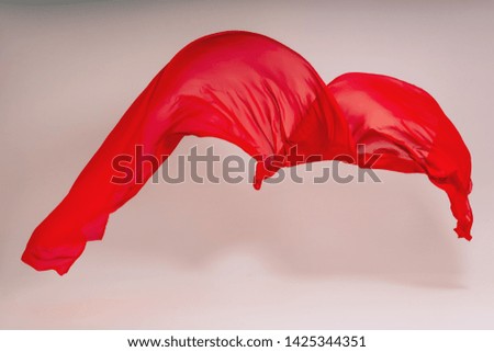 Red fabric on a white background. Levitation of red fabric in the photo studio. Soaring piece of cotton fabric. Flying colored fabric on a light background