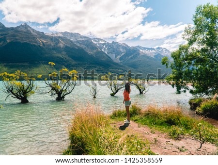 Woman walking to row of Willow Trees, on lake in Glenorchy. Beautiful landscape, with blue lake, mountains and clear sky. Nature, travel, tourism, outdoor concept. Shot near Queenstown, New Zealand   