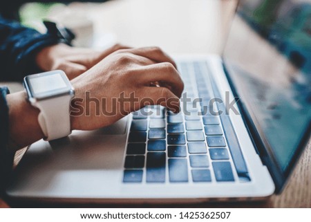 Side view of female hands with smartwatch keyboarding text on modern laptop in search information for course work.Freelancer working at modern computer using wireless high speed internet connection