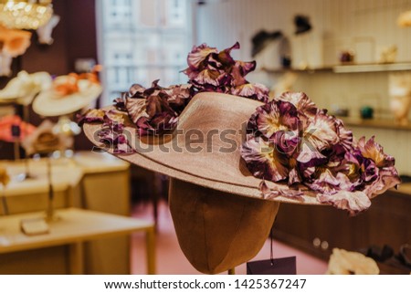 Beatiful hat decorated with flowers on display in focus with elegant hat store at background out of focus. Retail Shop Costume Dress Fashion Store Style Concept
