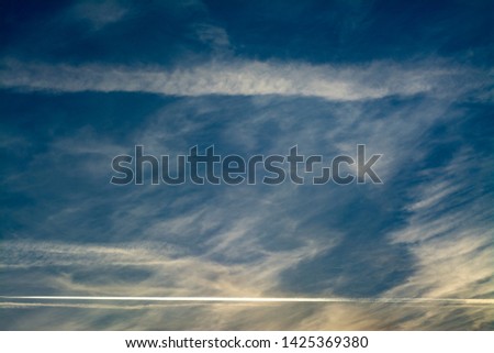 Clouds with jet trails from planes in the sunset sky with yellow reflections. Suitable for use as a background or cover for a book, report, presentations, slides, brochures, flyers, advertising poster