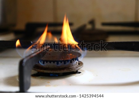 Close-up picture of old and dirty black gas stove burner with blue and orange flames burning for cooking.
