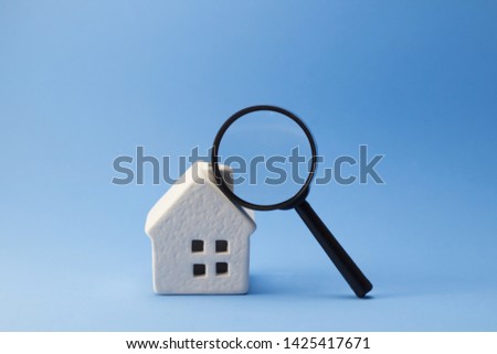 Miniature of white house with magnifying glass standing on blue background,Find real estate, searching for home 
