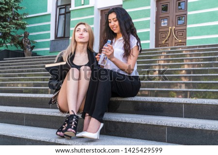 portrait of two beautiful students with a book and a bottle of water in hand, sitting on the steps of the university