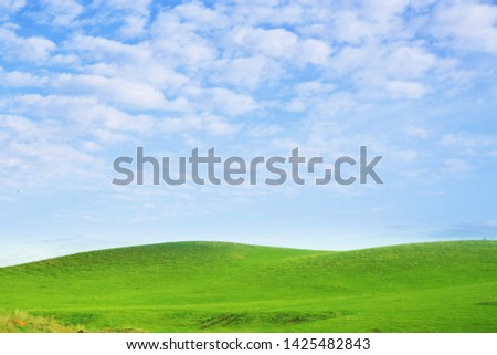 White fluffy clouds in the blue sky and green hills.
