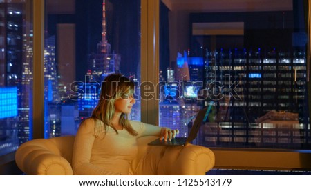 CLOSE UP: Caucasian woman on a business trip sits in her hotel room with a spectacular view of NYC at night and works on her computer. Student working on her project from hotel room above Times Square