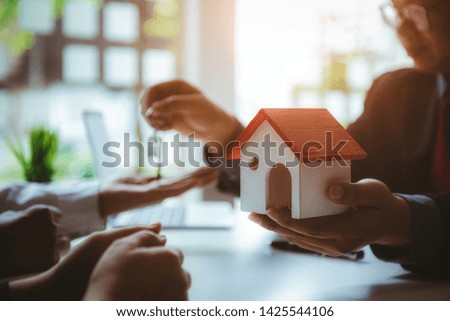Closeup hands of real estate agent give house model and house key to home ownership for young couple. Business successful contract concept.