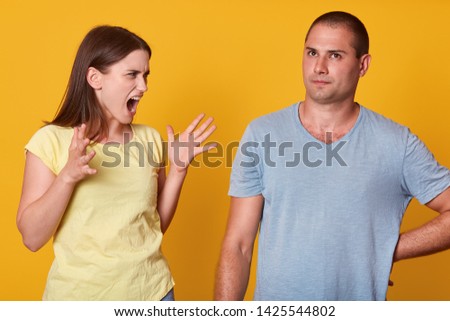 Image of screaming angry woman raising her hands, having quarrel with her husband, looking at him with anger. Calm slender man listening to shout, trying not to react, keeping silent. Family life.