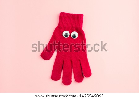 top view red  glove  with googly eyes isolated  on a pink background
