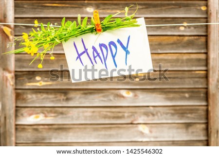 The inscription happy on white paper, fastened with a clothespin to a rope against the background of a wooden wall