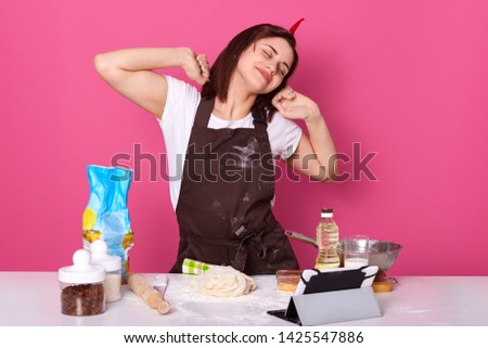 Happy housewife or baker stretching hands after tired day in kitchen, finishes kneading dough with enjoyed facial expression. Studio picture isolated over pink background. Homemade pastry concept.