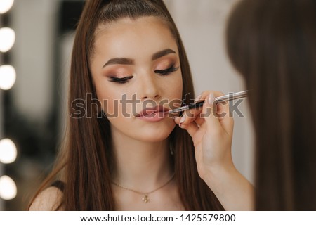 Makeup artist applies lipstick. Hand of make-up master, painting lips of young beauty redhead model. Make up in process Royalty-Free Stock Photo #1425579800