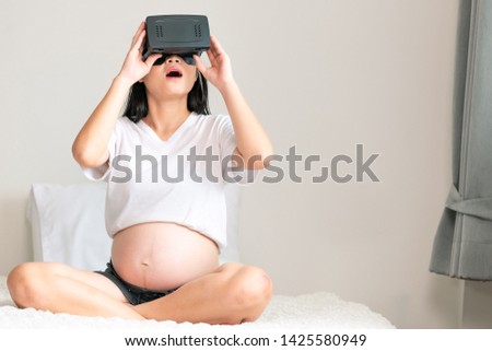 Asian pregnant woman using virtual reality goggle in bedroom. Very surprise and exciting mood.