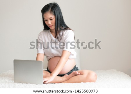 Asian pregnant woman using laptop in bed. Focus mood. With copy space.