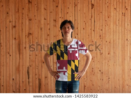 Man wearing Maryland flag color shirt and standing with akimbo on the wooden wall background, the states of America.