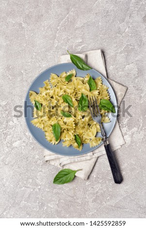 Top view of tasty farfalle pasta with pesto sauce and basil leaves on gray concrete background