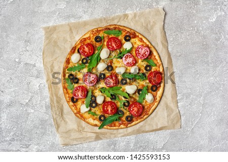 Top view of round pizza with tomato, cheese, olives and arugula leaves for vegetarians on gray concrete background