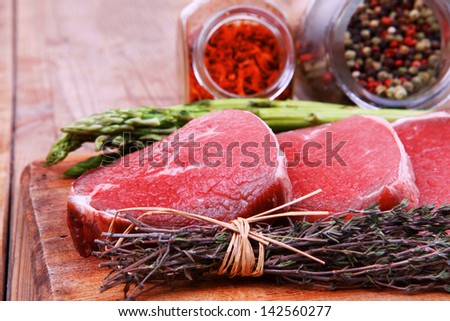 meat food : raw beef fillet on cutting board with asparagus and thyme bundle , with color peppercorn mix and red paprika powder mixed with dry spices ready to cooking