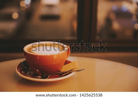 Latte art coffee with bread in a red cup on a wooden table and background bokeh outside the window