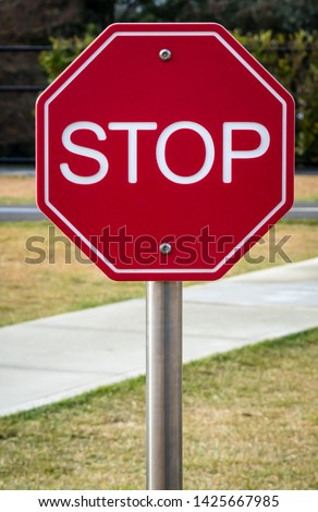 Plastic red and white hexagon sign with text STOP in front of grass and sidewalk in play area