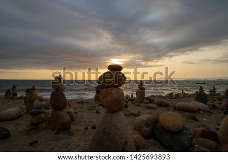 Balancing rock stones on a beautiful. romantic sandy beach with the sun setting in the backgrounds under the clouds, taken on the beach of Puerto Vallarta in Mexico