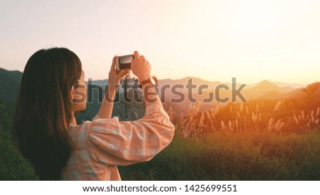Young asian woman taking a photo with her smartphone in beautiful mountain view and sunset golden hour, banner style for background and copy space