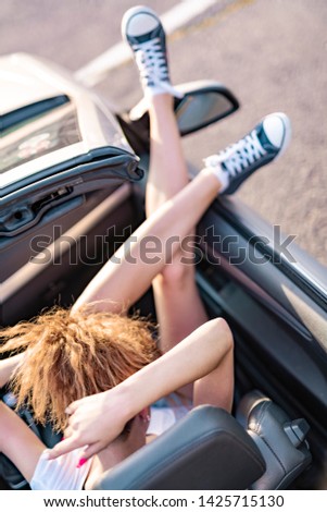 Dazzling young girl posing in a convertible car. Focus on hair on a model.