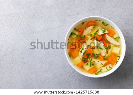 Chicken soup with vegetables in white bowl. Grey stone background. Copy space. Top view.